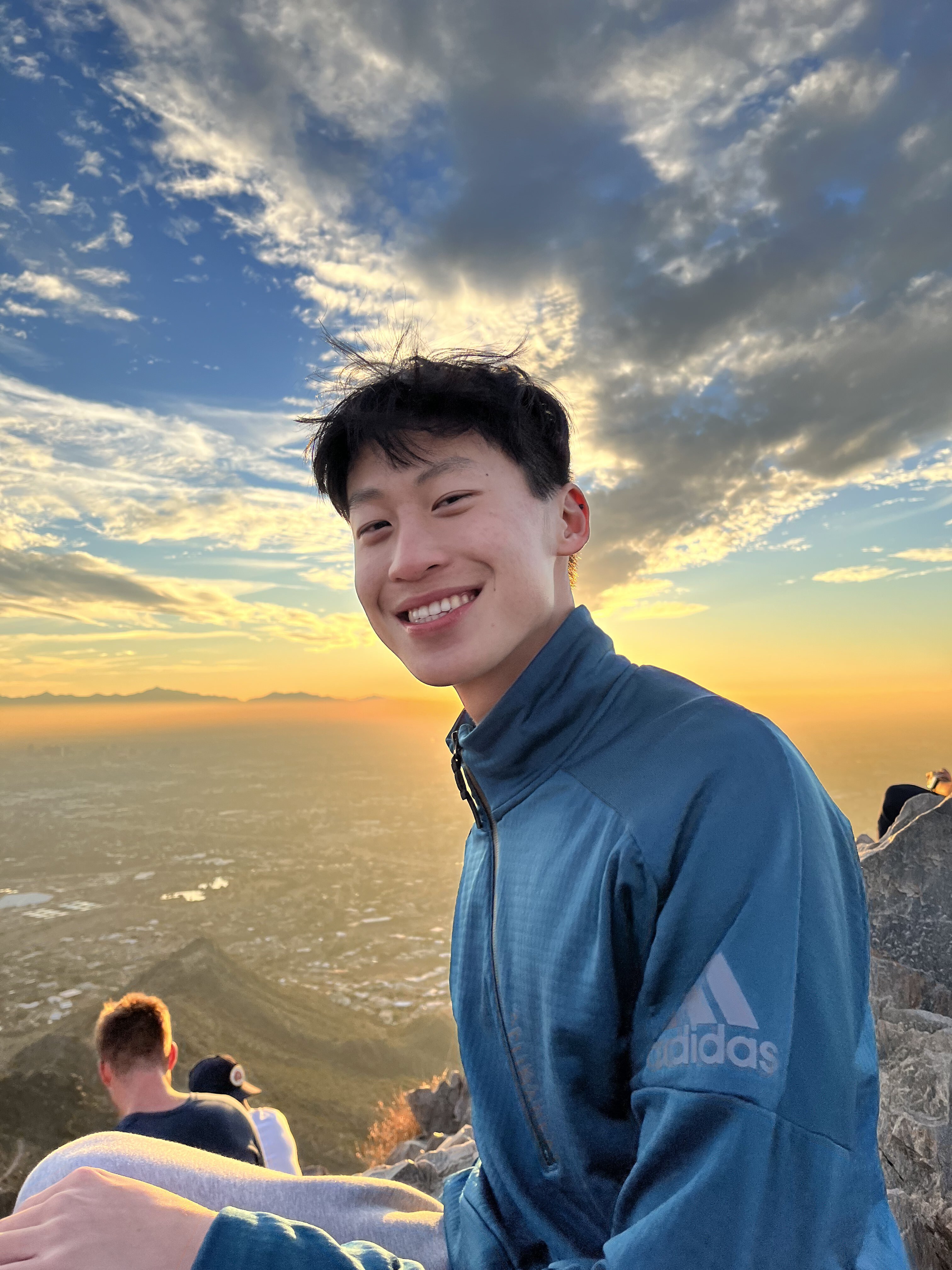 headshot of Geoffrey, an asian man, looking over a large body of water with colorful sky